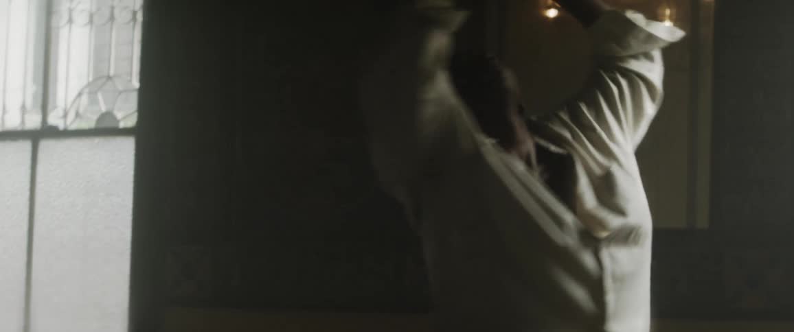 Young man wearing a white shirt dances spinning inside a dimly lit room