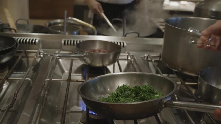 Alcohol is poured over greens then lit while pan is shaken
