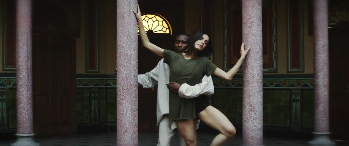 A man and woman are doing an expressive dance between pillars of an old building
