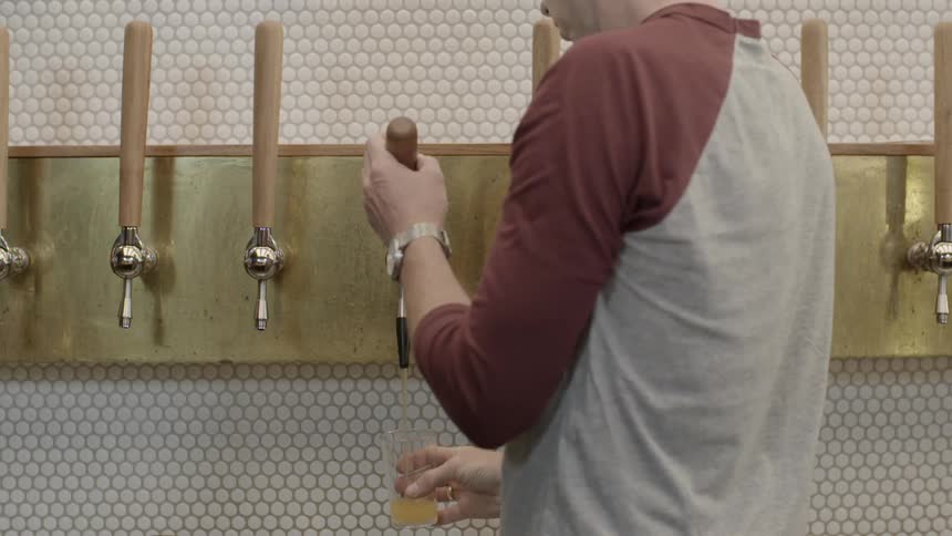 Man pouring amber liquid from a tap into a class