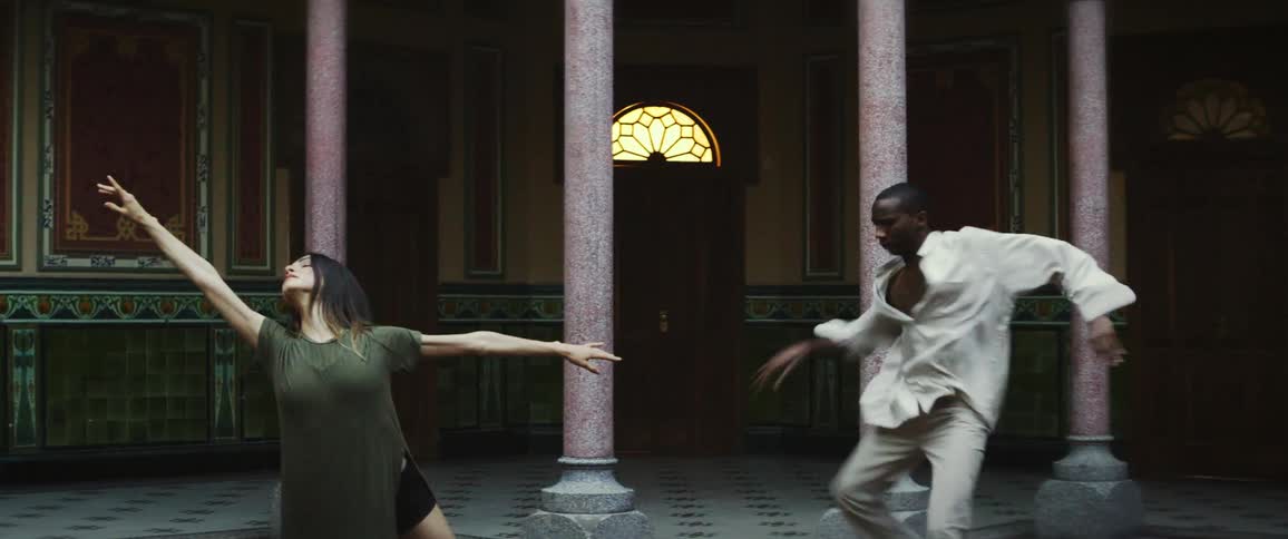 Male and female dancers dance near ornately decorated columns and tiles