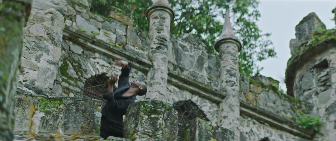 Male danver wearing black shirt and pants dances barefoot on top of castle tower