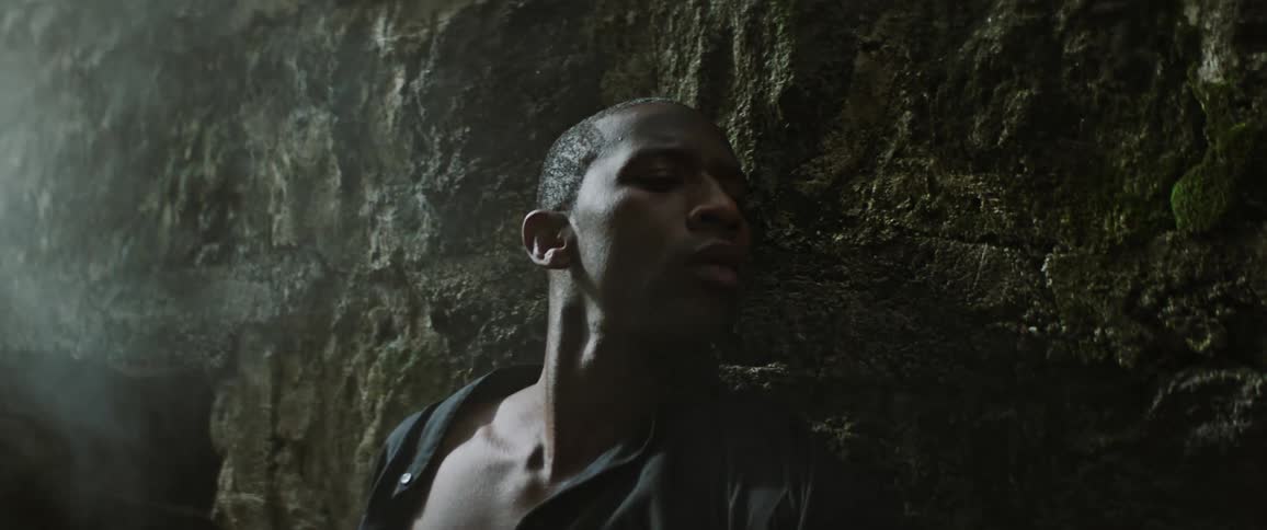 Tired young man wearing a black shirt reclines on the rock wall of a castle