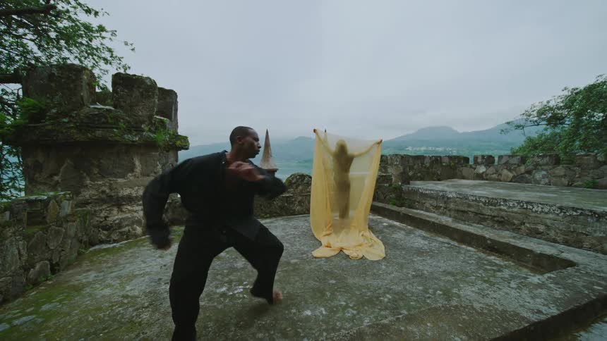 Woman covered in a yellow veil dances with a man dressed in black on a castle