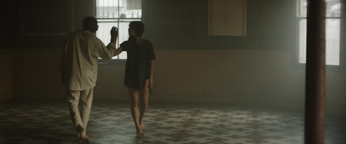 Woman in a short black dress dancing with a man dressed in white inside a dimly lit room