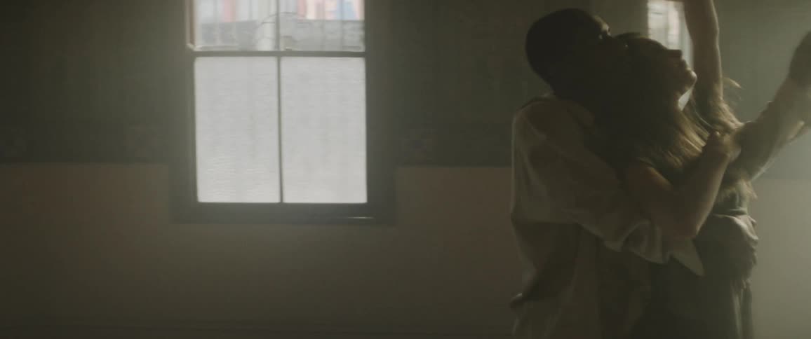 Woman in a short black dress dancing with a man dressed in white inside a dimly lit room