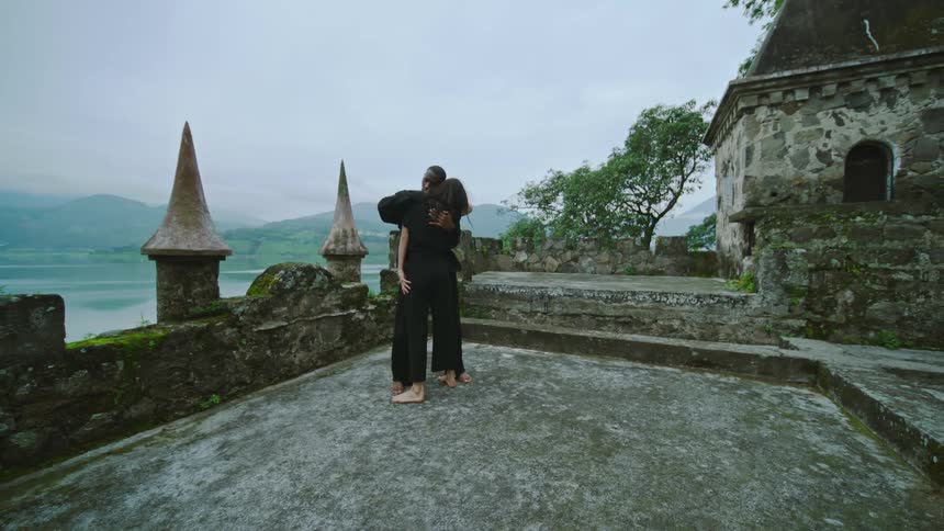 A couple wearing black clothes dancing on the rooftop of a castle near a lake