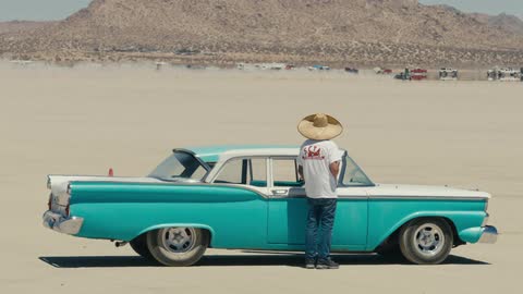A man is standing outside of his car in the desert