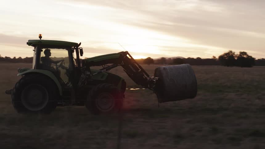 A man drives a tractor carrying a hay bail across a field