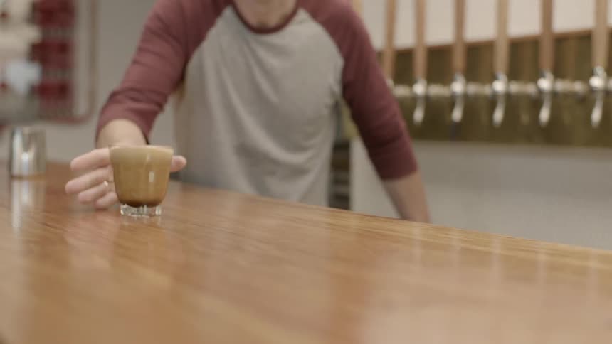 A man slides a beverage across a wooden bar