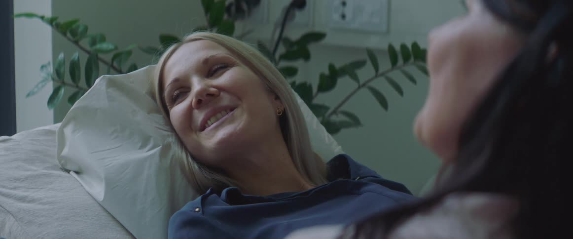 Pregnant patient sits on bed looking toward screen with ultrasound technician