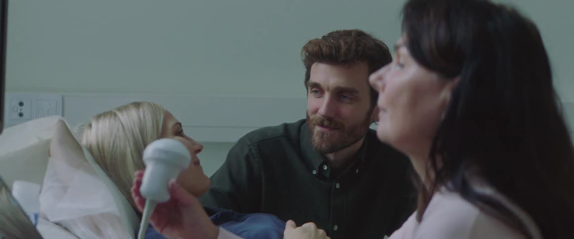 Ultrasound technician grabs wand as man sits next to pregnant wife