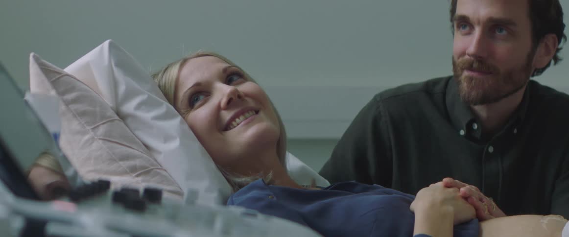 A pregnant woman is laying down with her belly exposed as a man sits next to her in a doctors office