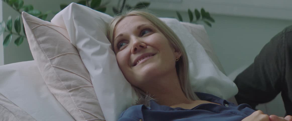 A woman smiles and looks up as she lies in a hospital bed