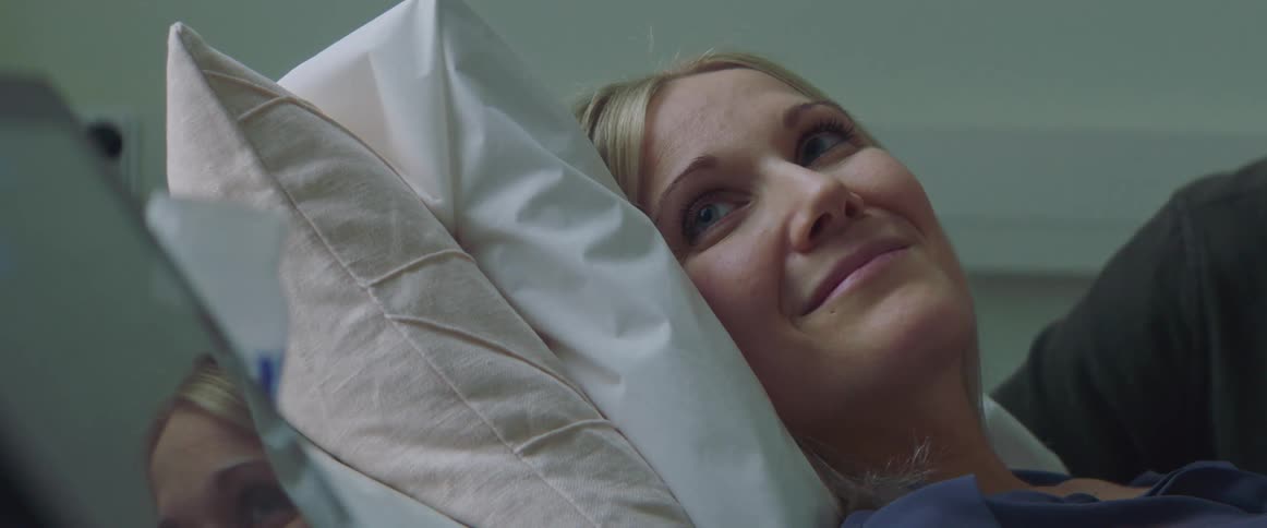 A woman is laying down and smiling as she looks at a monitor