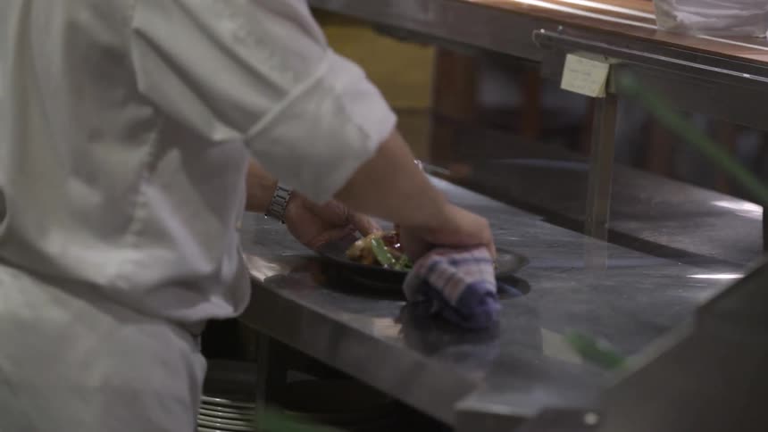 A chef is preparing a dish wiping a plate