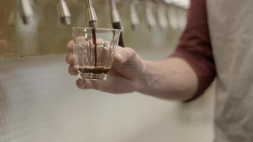 Beer is being poured into a small glass from a spout