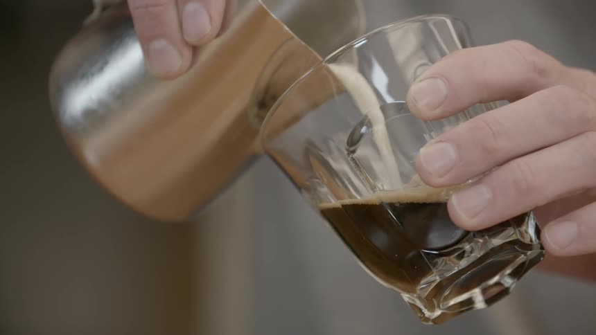 Cream is carefully poured into a glass of brown liquid