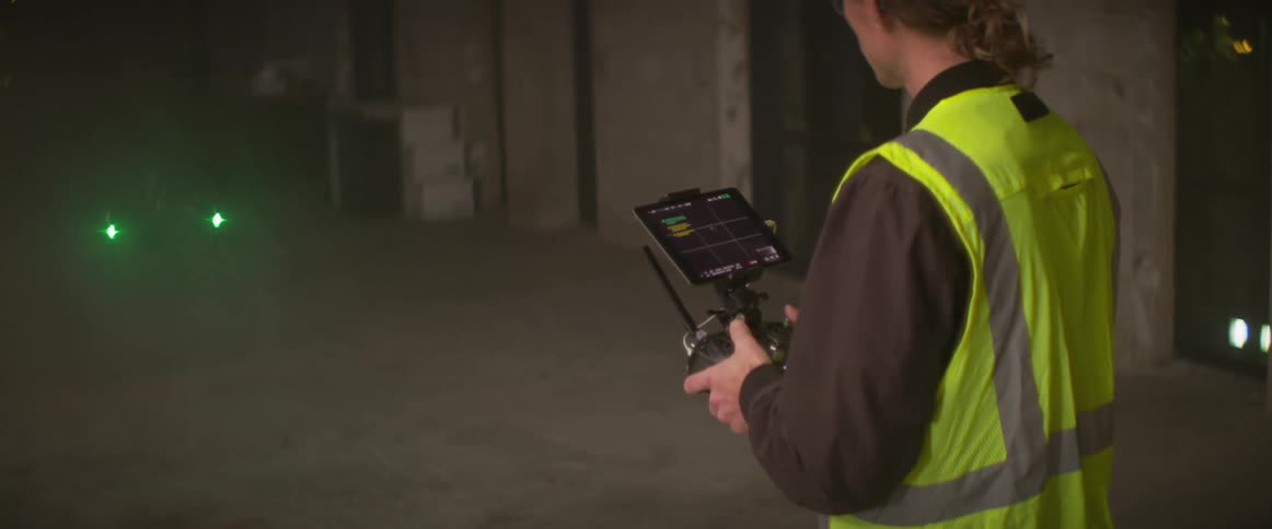 Construction worker wearing a yellow vest controles a drone flying inside a building at night