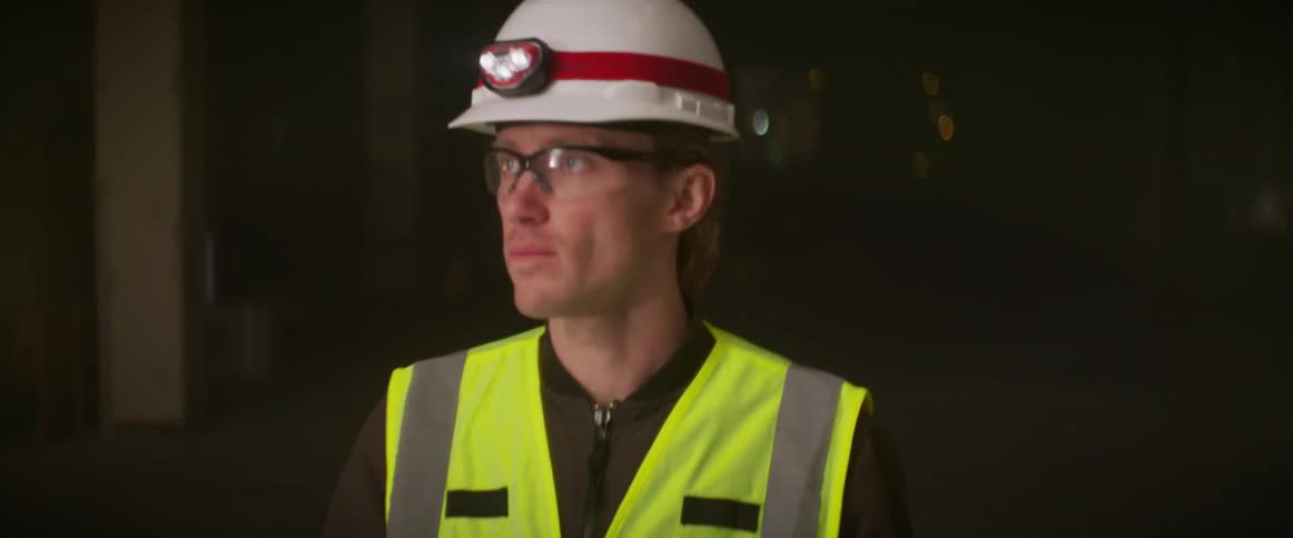 Construction worker wearing bright yellow vest and white hardhat supervising a construction site at night