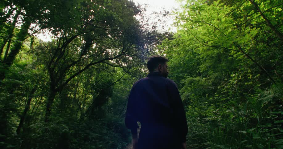 A man stands looking left and right at the surrounding trees and bushes