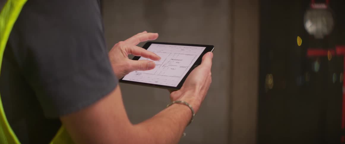 Worker consults diagram on tablet while examining machine