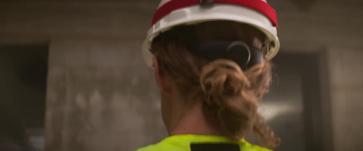 Man wearing hardhat and safety vest talks while consulting diagram on tablet