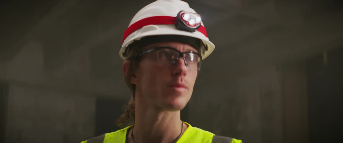 A construction worker stands in a building and points around the room as he talks