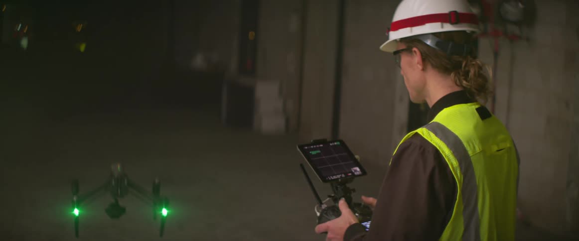 Construction worker wearing a yellow vest controles a drone flying inside a building at night