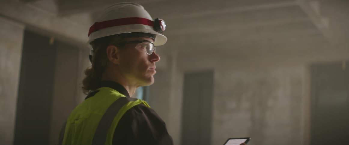 A construction worker looks at at tablet as he walks through a construction site