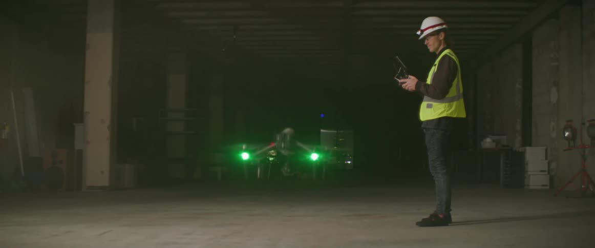 Construction worker wearing a yellow vest controles a drone flying inside a building at night