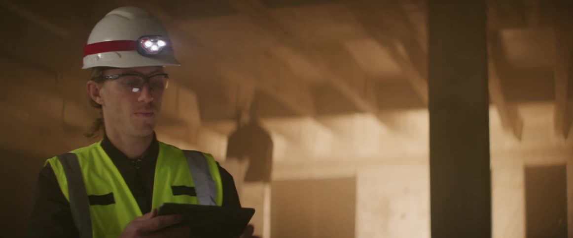 A man nods and points to the ceiling while holding and looking at a tablet