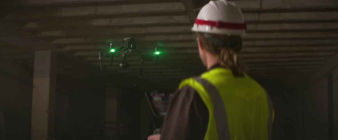 A man in a hard hat and safety vest controls a drone inside a building