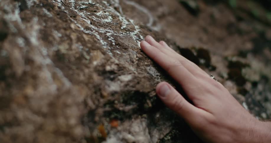 A man runs his hand down rock on a cliff