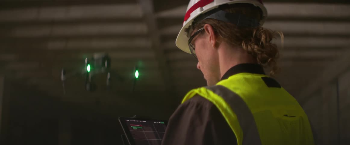 A man in a safety vest controls a drone inside a building