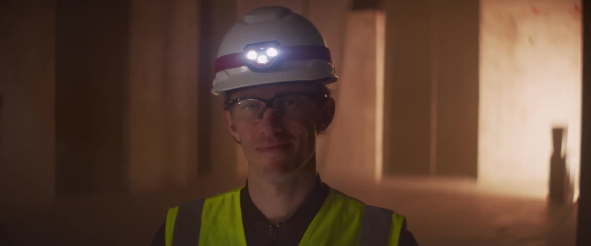 A man wearing a hardhat with head lamp stares straight ahead