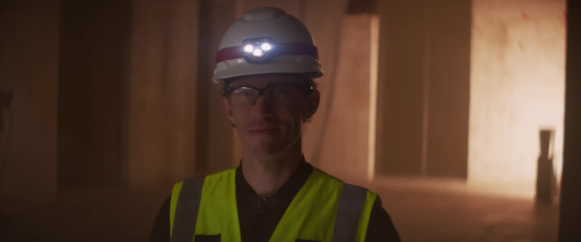 Worker wearing lit headlamp on his hard hat stands in shadowy building
