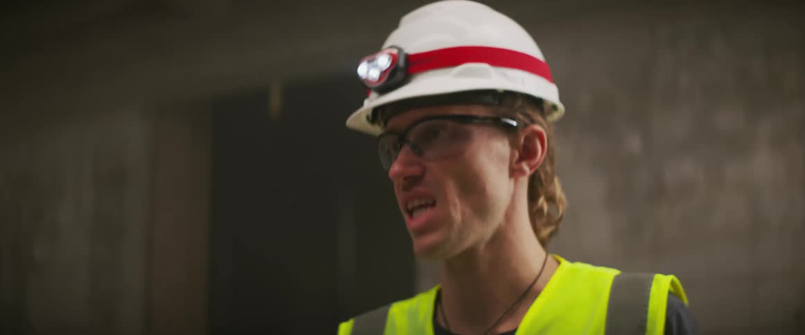 Construction worker wearing bright yellow vest and white hardhat supervising a construction site at night
