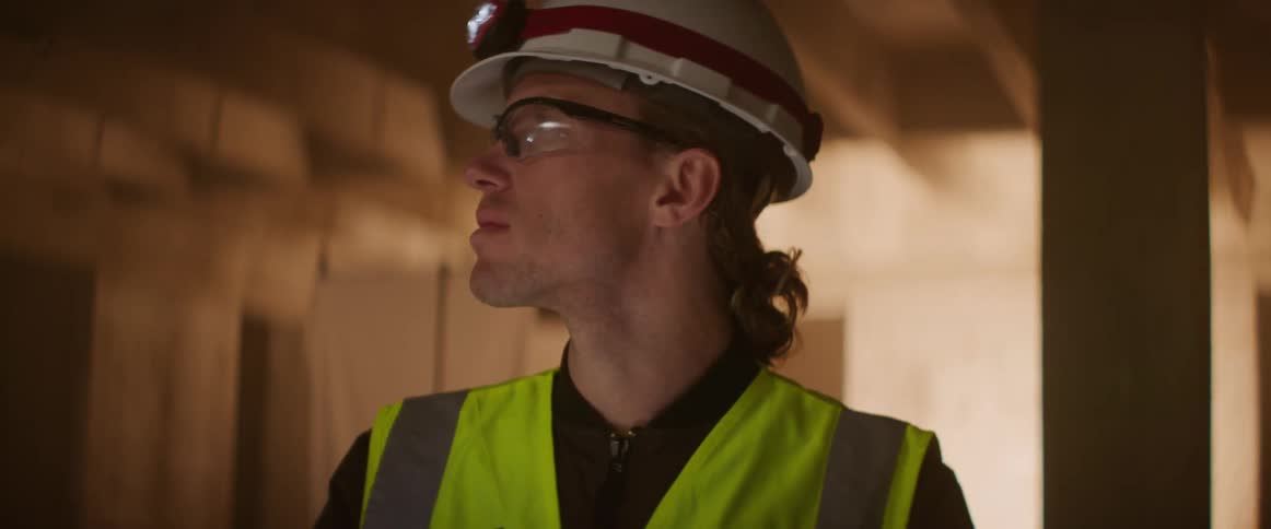A man wearing a hardhat with light and safety goggles looks up and around