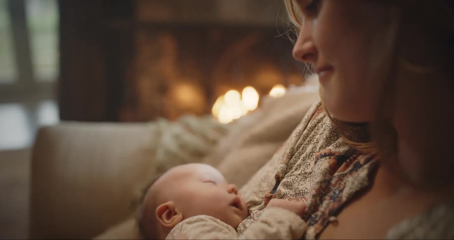 A woman cradles a sleeping baby while sitting on a sofa indoors