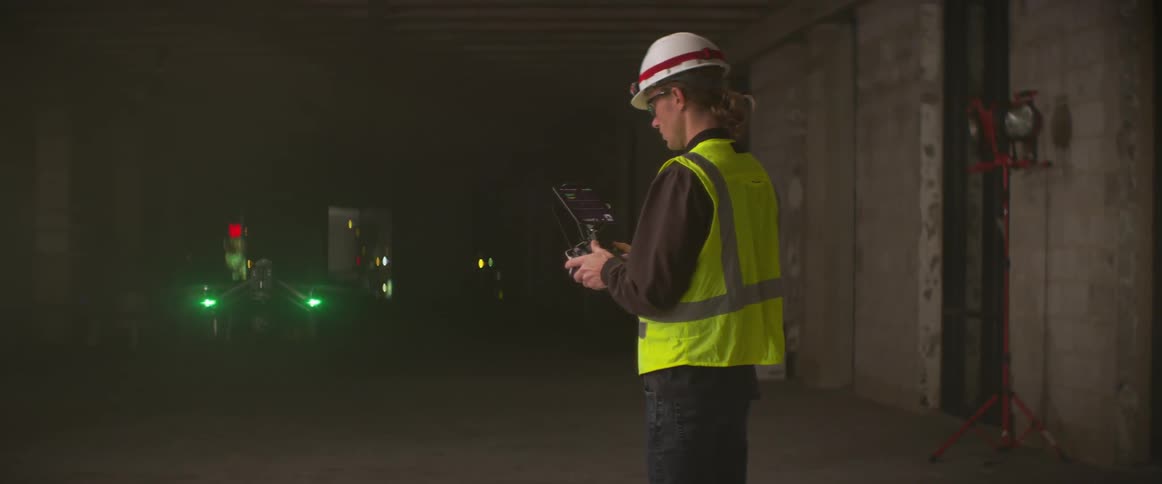 A construction worker flies a drone in the dark building