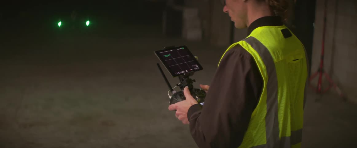 Worker wearing hard hat and safety vest manipulates drone while standing in work site
