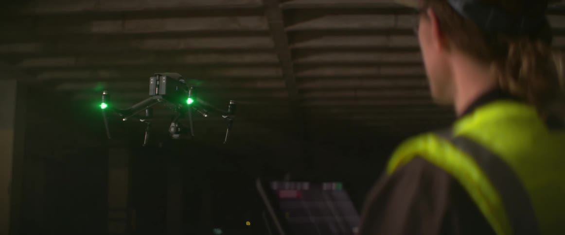 A construction worker looks at a tablet as he controls a drone in a building