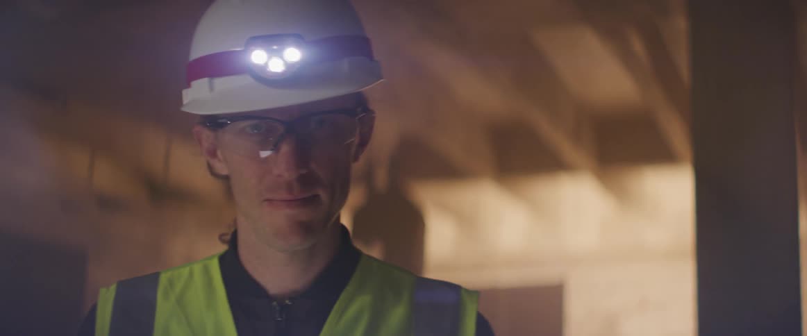 A construction worker holding cell phone turns around in a building being built