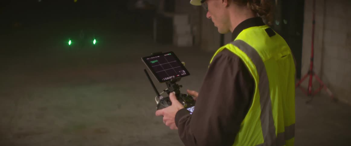 Worker wearing a safety vest guides drone along floor in building