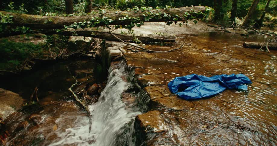 Blue plastic canvas flows along river passing through forest and down waterfall