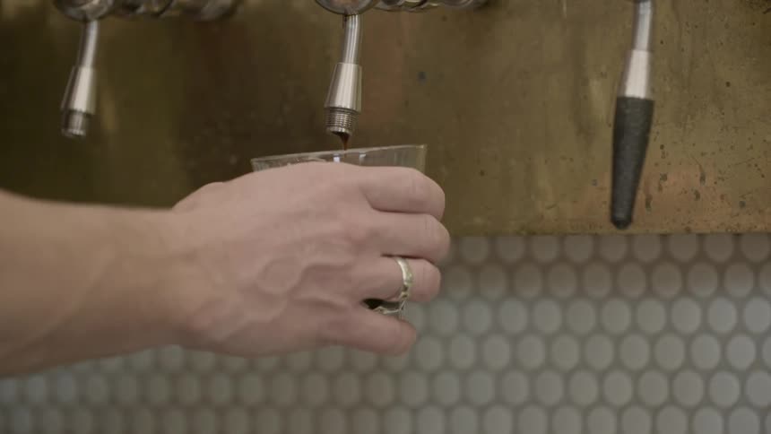 A brown liquid goes into a glass from the tap