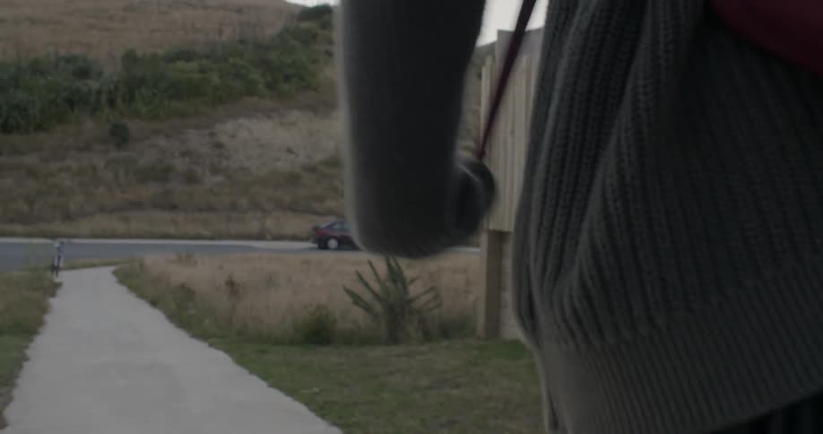 A person is walking down the sidewalk toward some hills