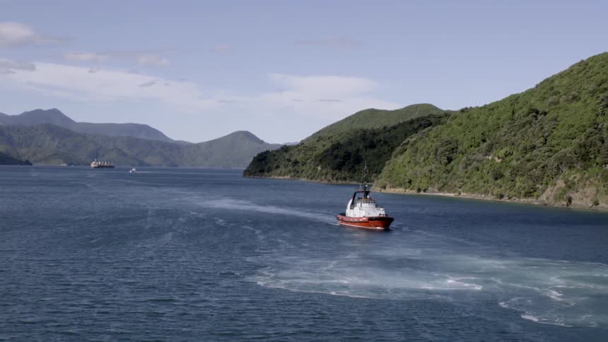 A boat moves up a body of water surrounded by green hills