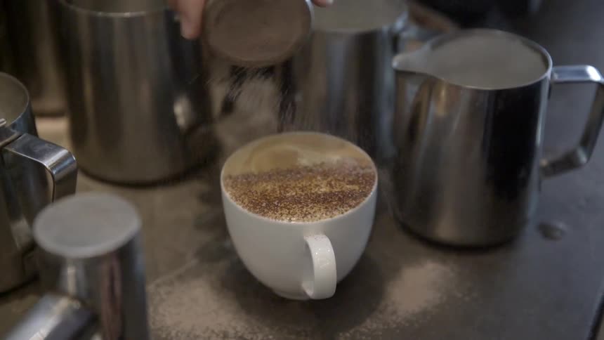 Cinnamon is poured on a cup of coffee